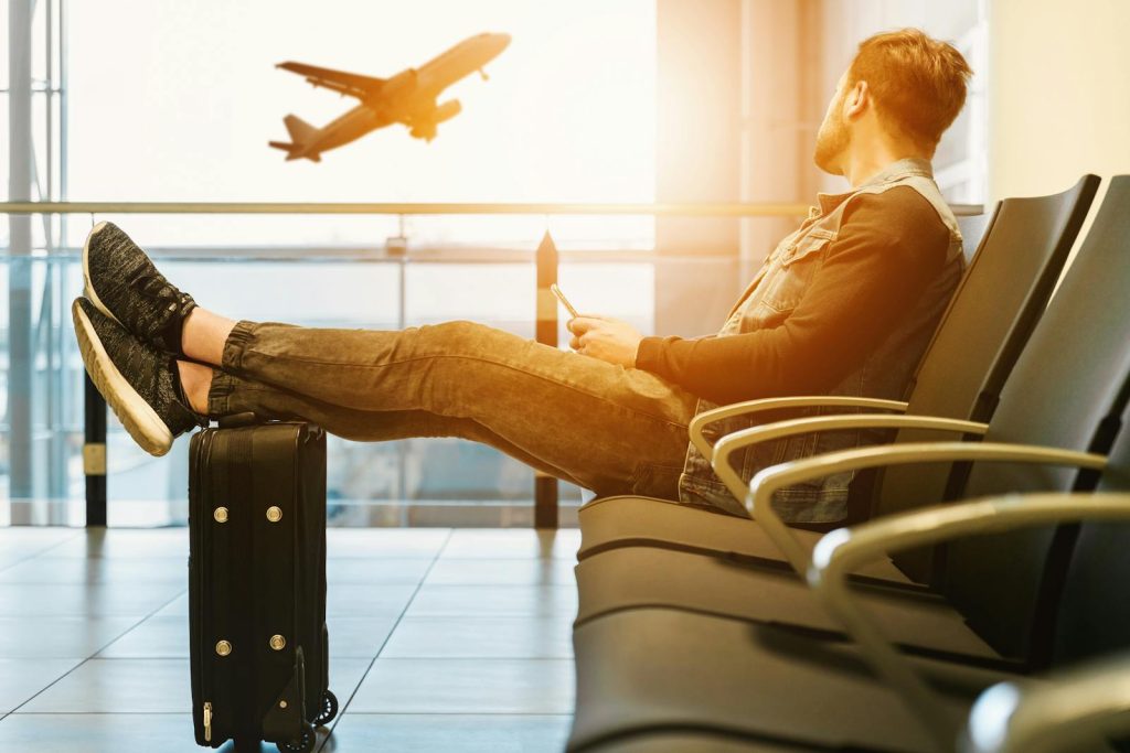 Traveler relaxes at airport while waiting for flight boarding, with plane taking off in background.