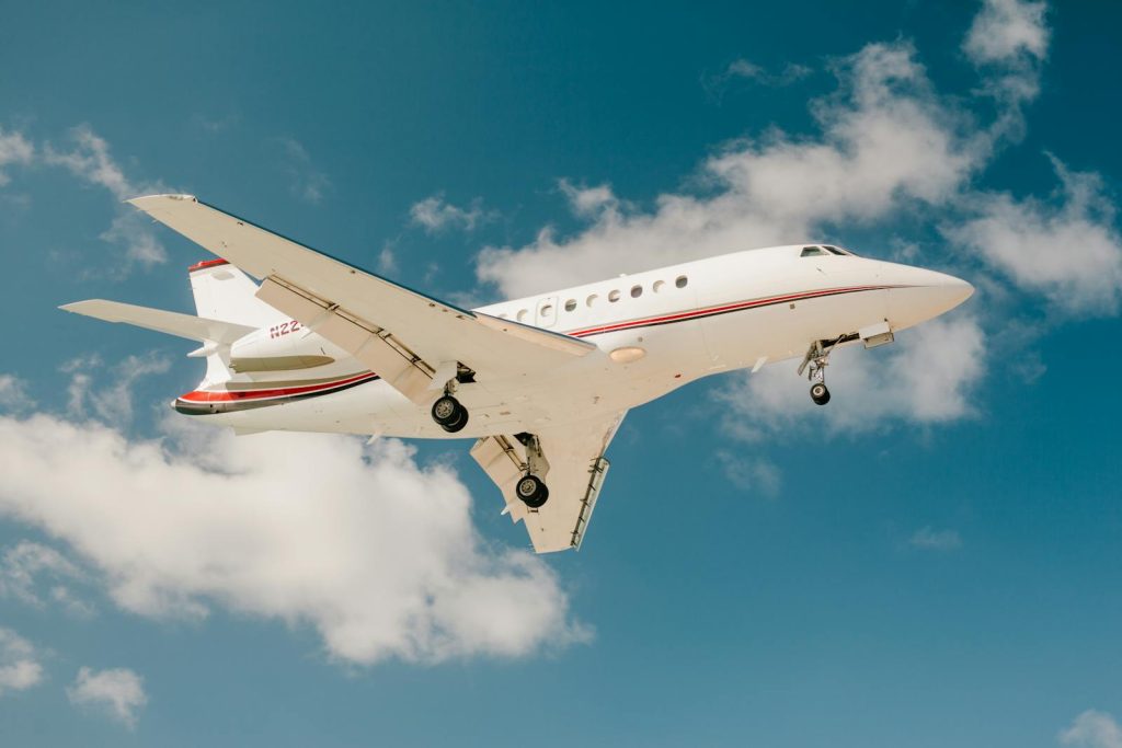 A sleek private jet captured mid-flight against a vibrant blue sky with scattered clouds.